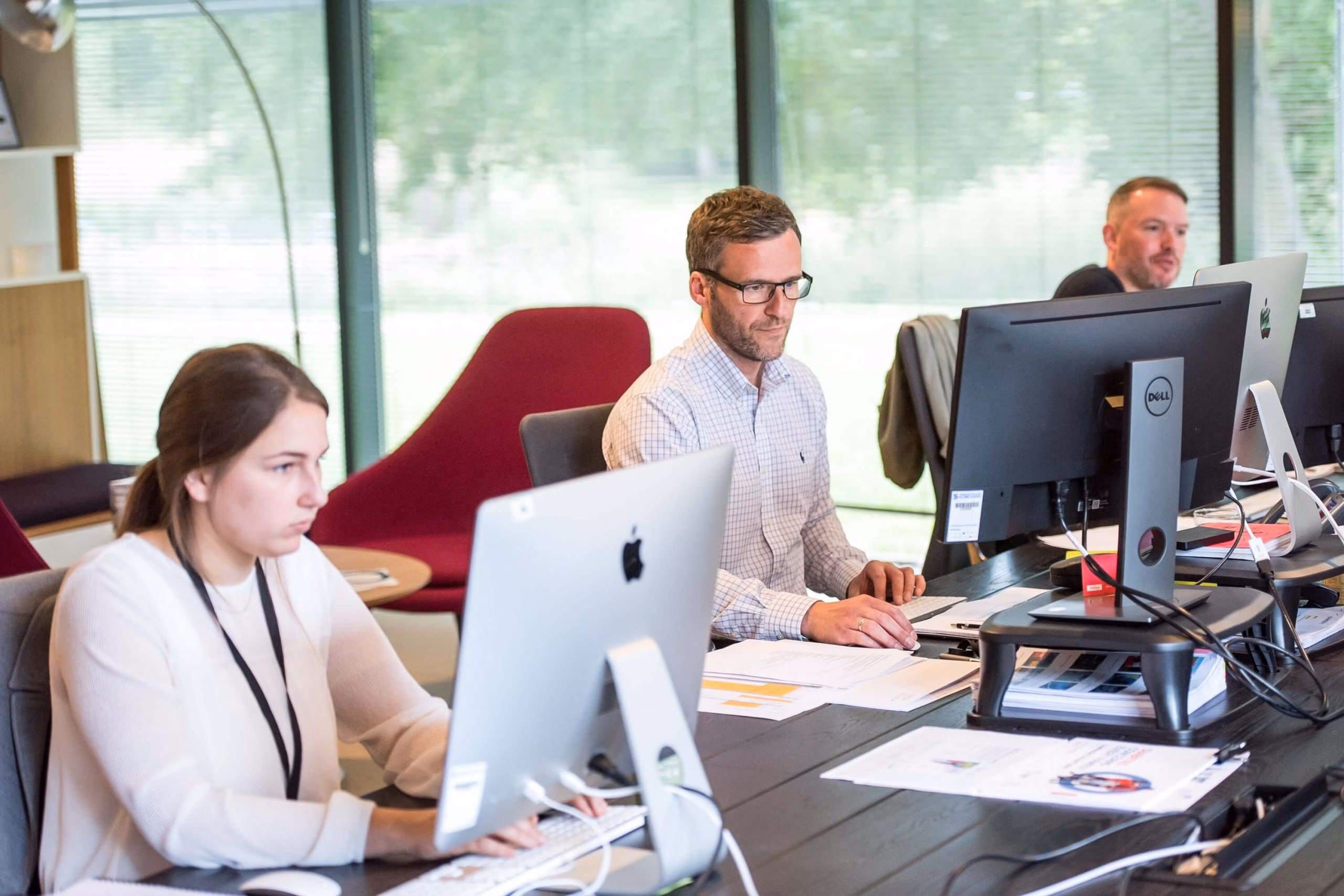 Group of people working together on computers in a professional office setting, focused on tasks and collaboration.