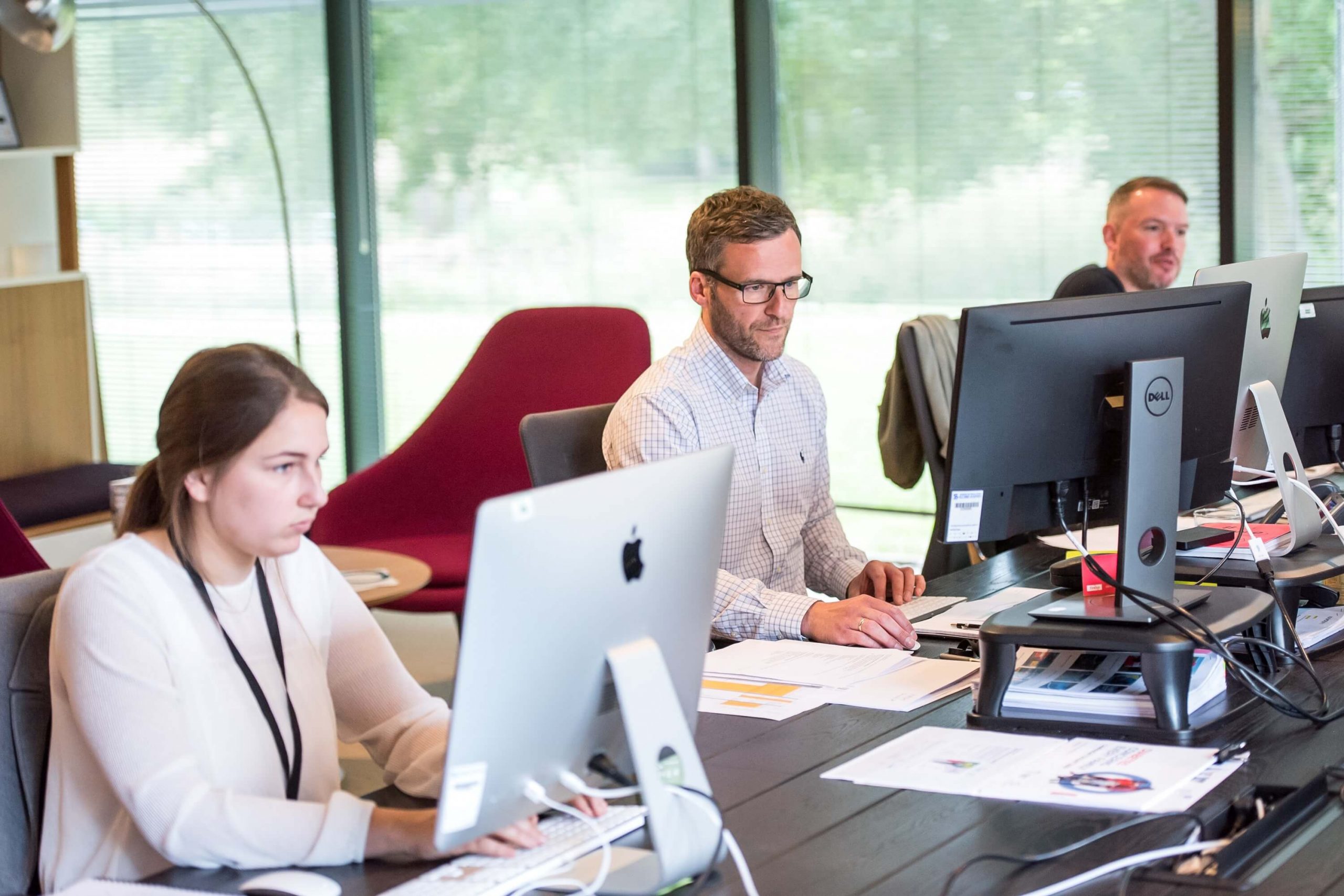 Group of people working together on computers in a professional office setting, focused on tasks and collaboration.